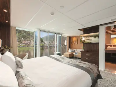 Helle, moderne Suite auf der AMADEUS Queen mit Doppelbett, Sitzbereich und raumhohen Fenstern. 