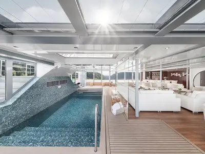 Schiffsinterieur: Lichtdurchflutete Lounge mit Mosaik-Innenpool und weissen Sofas auf der AMADEUS Queen. Bar und Panoramafenster mit Blick auf grüne Berge. 