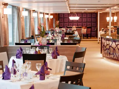 Elegantes Restaurant auf der AMADEUS Silver II mit vielen Tischen, weiß gedeckt und lila Servietten. 