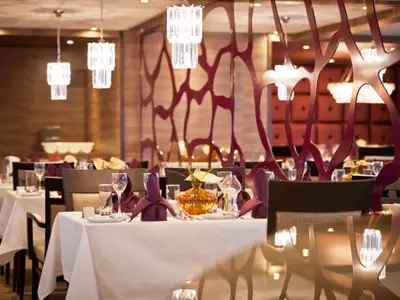 Elegantes Schiffsrestaurant auf der AMADEUS Silver II. Gedeckte Tische mit weißen Tischtüchern, violetten Servietten, Gläsern und Blumendeko. Rote Raumteiler und Leuchter. Gehobene Atmosphäre.