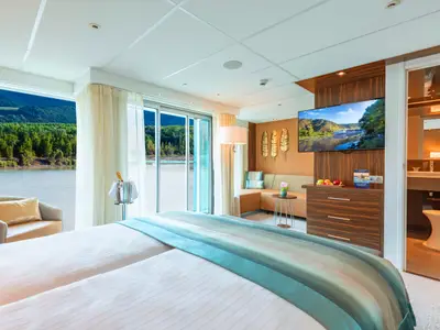 Helle Suite auf der AMADEUS Star mit Flussblick, modern eingerichtet, Bett, Sofa, TV und Badzugang.