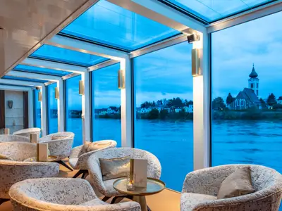 Moderne Lounge auf der AMADEUS Star mit Panoramafenstern und Flussblick bei Dämmerung.