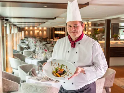 Chef präsentiert ein elegantes Gericht im stilvollen Restaurant an Bord der AMADEUS Star.