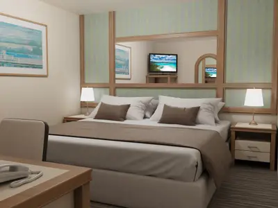 Eine helle, modern eingerichtete Kabine der Carnival Adventure mit einem gemachten Doppelbett. Links ein Schreibtisch mit Telefon, rechts ein Nachttisch mit Lampe. Über dem Bett eine Spiegelfläche mit Fernseher und Wandverkleidung.