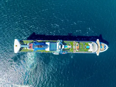 Vogelperspektive auf die große Carnival Adventure. Das Oberdeck bietet mehrere Pools, zahlreiche Sonnenliegen, grüne Bereiche und blaue Wasserrutschen, umgeben von tiefblauem Meer.