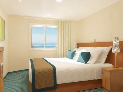 Moderne Außenkabine auf der Carnival Breeze mit Doppelbett, blauen Kissen und Holzmöbeln. Ein großes Fenster bietet Blick auf Meer und bergige Küstenlinie am Tag.