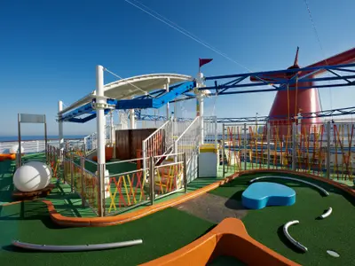 Ein bunter Minigolfplatz auf dem Oberdeck der Carnival Breeze mit Blick auf das weite blaue Meer und den markanten roten Schornstein. Keine Personen.