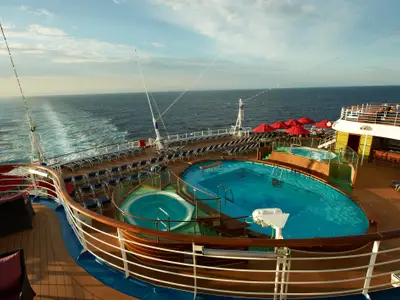 Blick von oben auf das Pooldeck der Carnival Breeze mit Pools, Whirlpool, Liegestühlen und Bar. Dahinter das offene Meer.