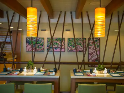 Einladendes, asiatisch inspiriertes Restaurant an Bord der Carnival Breeze mit kunstvollen orangefarbenen Deckenlampen, Bambus-Trennelementen und Tischen, die für Mahlzeiten gedeckt sind.