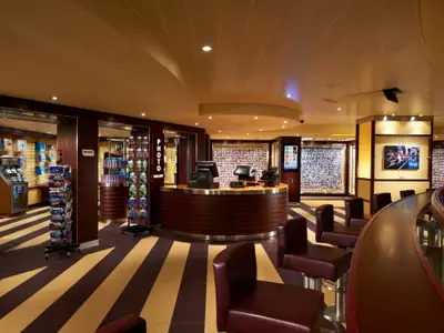 Innenansicht der Foto-Galerie der Carnival Breeze. Ein Tresen, Fotoauslagen und eine Bar mit Ledersitzen. Der Boden hat ein markantes Streifenmuster.