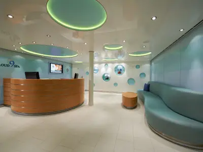 Moderner Empfangsbereich des Cloud 9 Spa auf der Carnival Breeze. Ein geschwungener Holz-Tresen, eine lange blaue Sitzbank und runde Deko-Elemente.