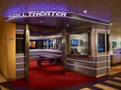Eingangsbereich des Thrill Theaters an Bord. Roter Teppich, Showzeiten, Filmplakate und ein Ticket-Schalter sind beleuchtet.