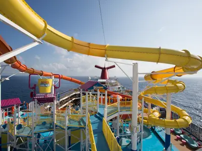 Blick von oben auf den AquaPark mit bunten Wasserrutschen und einem kippenden Eimer auf dem Deck der Carnival Breeze. Das Meer ist im Hintergrund sichtbar.
