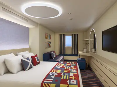 Moderne Außenkabine auf der Carnival Celebration mit Doppelbett, blauer Schlafsofa, Marinedekor und seitlichem Fensterblick auf das Meer. Ein runder Spiegel mit Beleuchtung und ein großer Fernseher sind an der Wand montiert.