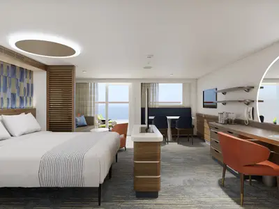 Ansicht einer modernen Suite auf der Carnival Celebration. Die Kabine verfügt über ein Doppelbett, einen Arbeitsbereich mit Stuhl und einen Esstisch. Ein Balkon bietet Meerblick.