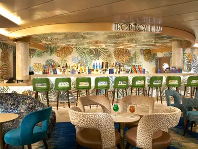 Die 'TROPICALE BAR' auf der Carnival Celebration mit leuchtenden Mosaikwänden in Blatt-Motiven, grünen Barhockern und bequemen Lounge-Sesseln. Eine Auswahl an Spirituosen ist an der Bar zu sehen.