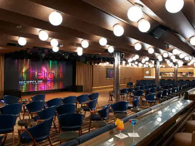 Innenansicht des Limelight Nightclubs auf der Carnival Celebration. Die LED-Leinwand zeigt den Schriftzug "Limelight Nightclub". Bequeme blaue Sessel und eine lange Bar mit bunten Cocktails füllen den Raum.