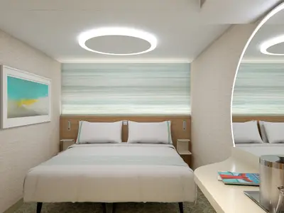 Moderne Innenkabine der Carnival Celebration mit Doppelbett, Nachttischen und einem beleuchteten Kunstwerk. Elegante, indirekte Beleuchtung am Kopfteil und an der Decke.
