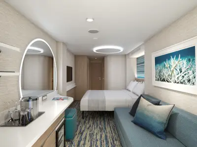 Helle, moderne Kreuzfahrtkabine mit Einzelbett, türkisfarbenem Sofa, ovalem Leuchtspiegel und Korallen-Wandbild. Beige Wände und blauer Teppich.