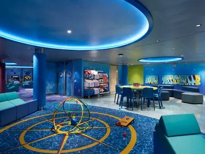 Geräumiger Kinderbereich mit blauen Wänden, runden Lichtinstallationen, bunten Sitzgelegenheiten, einem Maltisch und Spielecken. Mehrere Bildschirme zeigen Fische.