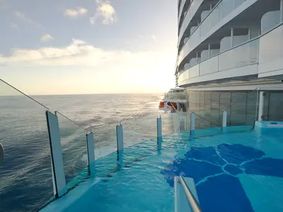 Infinity-Pool auf der Carnival Celebration mit Meerblick bei Sonnenuntergang. Gläserne Brüstung, weißer Schiffsrumpf und Balkone sind sichtbar.