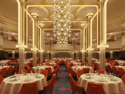 Ein luxuriöses, mehrstöckiges Hauptrestaurant auf der Carnival Celebration mit zahlreichen elegant gedeckten Tischen, orangefarbenen Stühlen und einer imposanten, goldenen Lichtinstallation in der Mitte. Der Raum ist von hohen, beleuchteten Säulen und einer Galerie umgeben, die ein weiteres Stockwerk mit Sitzgelegenheiten zeigt.