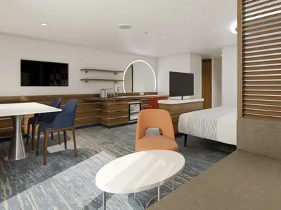 Eine moderne und geräumige Suite auf der Carnival Celebration. Die Suite verfuegt über einen Essbereich, einen Schreibtisch mit Spiegel, ein Sofa und ein Doppelbett. Sanfte Beleuchtung und Holzdetails dominieren.