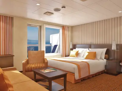 Geräumige Balkonkabine auf der Carnival Conquest mit Doppelbett, beiger Bettwäsche und orangen Akzenten, Sitzgelegenheiten, Fernseher und Meerblick durch große Fenster.