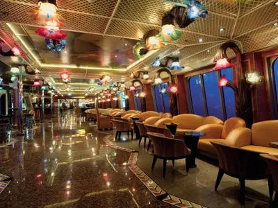 Luxuriöse Lounge der Carnival Conquest. Bunte Blumenlampen an der Decke, glänzender Boden. Gelbe Sofas und Sessel an großen Fenstern mit Blick aufs Meer.