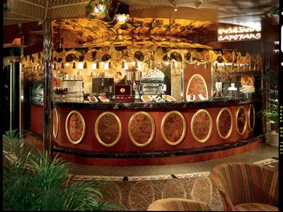 Opulente Schiffsbar oder Café mit dunklem Marmortresen, goldenen Ornamenten und Espresso-Maschinen. Auslage von Gebäck und Keksen. Warme, elegante Beleuchtung, ohne Personen.
