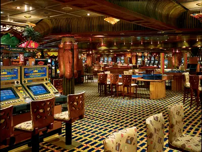 Ein aufwendig im Tiki-Stil dekoriertes Casino auf der Carnival Conquest mit zahlreichen Spielautomaten, Roulette-Tischen, Holzverkleidungen und geschnitzten Masken.