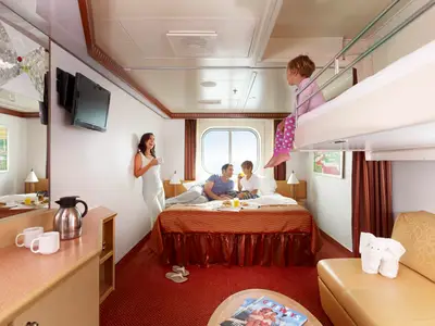 Eine Familie mit zwei Kindern genießt den Morgen in einer Kreuzfahrt-Außenkabine. Die Eltern und ein Kind sitzen auf dem Doppelbett, ein weiteres Kind auf dem oberen Hochbett. Ein Fenster bietet Meerblick.