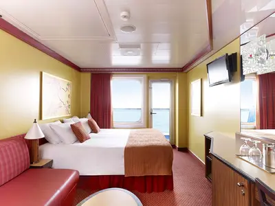 Balkonkabine der Carnival Dream mit Doppelbett, rotem Sofa, gelben Wänden und Meerblick durch Glastür zum Balkon. TV und Kommode sichtbar.