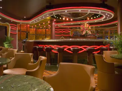 Moderne Bar-Lounge auf der Carnival Dream. Rote LED-Beleuchtung illuminiert Decke und Bartheke. Bequeme Ledersessel, grüne Marmortische und Barhocker. Ohne Personen.