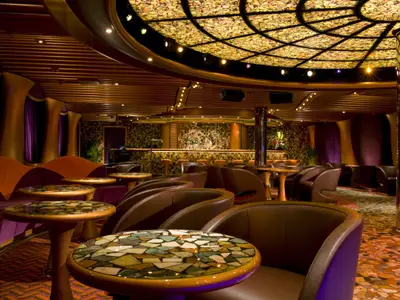 Luxuriöse Bar-Lounge auf der Carnival Dream mit Ledersesseln, Mosaiktischen und beleuchteter Bar im Hintergrund. Kunstvolle Decke.