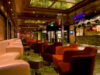 Elegante Lounge an Bord der Carnival Dream. Helle Ledersofas und rote Sessel. Eine Bar mit Fischskulptur und beleuchtetem WASABI-Schriftzug. Glänzende Böden.