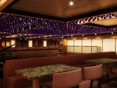 Eine luxuriöse Bar-Lounge auf der Carnival Dream. Die Szene zeigt dunkle Marmortische, bequeme rote Polsterbänke und Stühle. Im Hintergrund steht ein schwarzer Flügel, dahinter weitere Sitzbereiche. Die Decke ist mit einer auffälligen Installation aus zahlreichen violetten Kugeln geschmückt. Indirekte Beleuchtung schafft eine intime Atmosphäre.