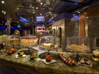 Eine elegante Desserttheke auf der Carnival Dream, reichlich gefüllt mit Kuchen, Torten, Cupcakes und Pralinen unter Glasglocken.