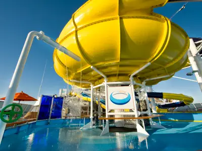 Ansicht eines riesigen gelben Wassereimers, der sich auf dem obersten Deck der Carnival Dream entleert. Im Hintergrund weitere Rutschen und Sonnenschirme. Der Himmel ist strahlend blau.