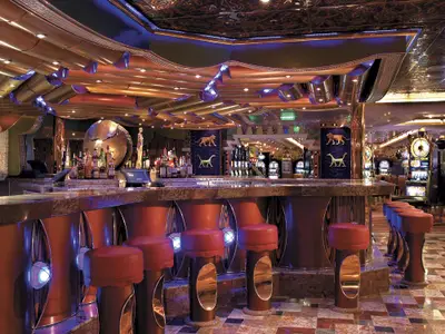 Luxuriöse Bar mit roten Hockern und Marmortheke auf der Carnival Freedom. Im Hintergrund beleuchtete Spielautomaten, goldene Deckenelemente und Tierfiguren.