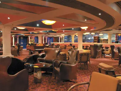 Eine elegant eingerichtete Bar-Lounge auf der Carnival Freedom mit zahlreichen braunen Ledersesseln und Couchtischen. Im Hintergrund sind ein Klavier und eine Bar mit Wandgemaelden zu sehen. Säulen stuetzen die Decke mit indirekter Beleuchtung.