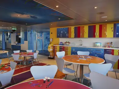 Geräumiger, bunter Kinderbereich auf der Carnival Freedom mit runden Tischen, Bastelmaterialien und einem M&M's-Charakter. Die Wände und Decke sind mit Unterwassermotiven bemalt.