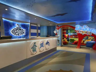 Empfangsbereich des Kinderbereichs Camp Ocean mit U-Boot-Logo und drei Altersgruppen-Logos. Rechts der Eingang zum Dr. Seuss Bookville, farbenfroh mit Figuren wie Cat in the Hat und Sitzsäcken.