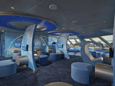 Ein moderner, blauer Kinderbereich auf der Carnival Freedom mit interaktiven 'SHARK'-Bildschirmen, bequemen Hockern und Ladesäulen sowie Fenstern.