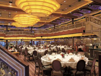 Großes, elegantes Hauptrestaurant der Carnival Freedom, festlich gedeckte Tische, hohe Decken, aufwendige Beleuchtung und verzierte Geländer. Fenster mit Meerblick im Hintergrund.