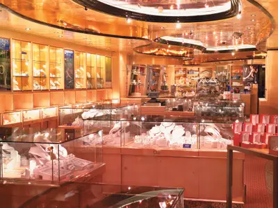 Innenansicht eines luxuriösen Duty-Free-Shops an Bord der Carnival Freedom, gefüllt mit Vitrinen voller Schmuck, Uhren und Designerhandtaschen. Die Decke ist goldfarben und spiegelt die Lichter wider.