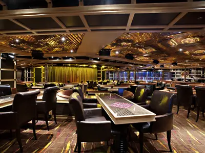 Blick in eine weitläufige, elegante Bar-Lounge an Bord der Carnival Glory mit dunklen Ledersesseln, Holztischen und einer auffälligen goldenen, reflektierenden Decke.