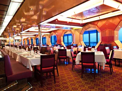 Ein leeres, elegantes Restaurant auf der Carnival Glory mit zahlreichen eingedeckten Tischen und roten Stühlen. Große Fenster bieten einen weiten Blick auf das blaue Meer.