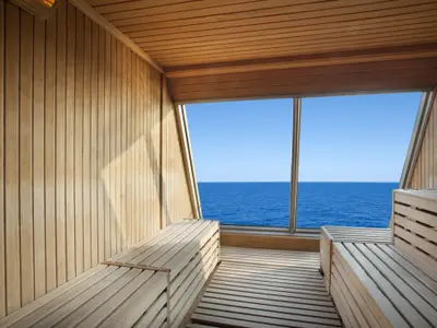 Innenansicht einer modernen holzgetäfelten Sauna auf der Carnival Glory. Großes Panoramafenster bietet weiten Blick auf das blaue Meer und klaren Himmel. Mehrere Holzsitze im Raum.