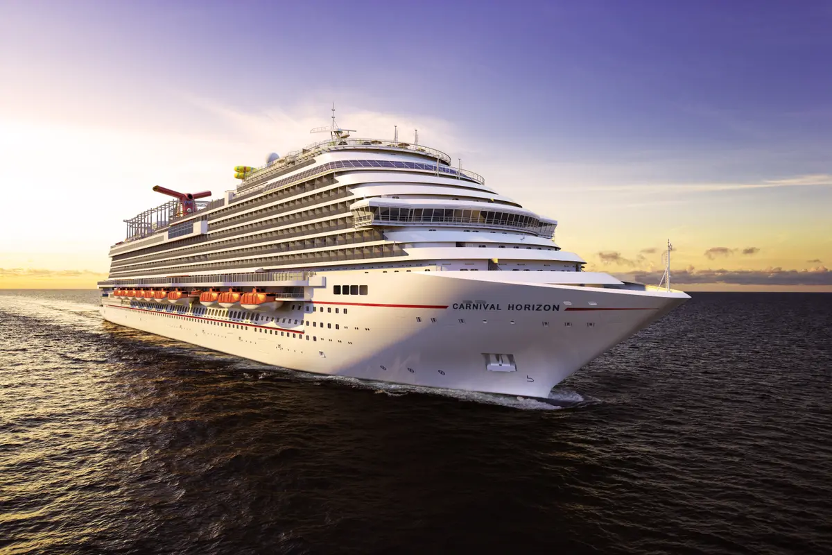 Die große Carnival Horizon fährt auf dem Meer in einem sanften Sonnenuntergang. Ihr Bug zeigt nach rechts, ihr Heck nach links, mit deutlicher Heckwelle. Orange-rote Rettungsboote sind an ihrer Seite sichtbar. Der Himmel ist in Pastellfarben.